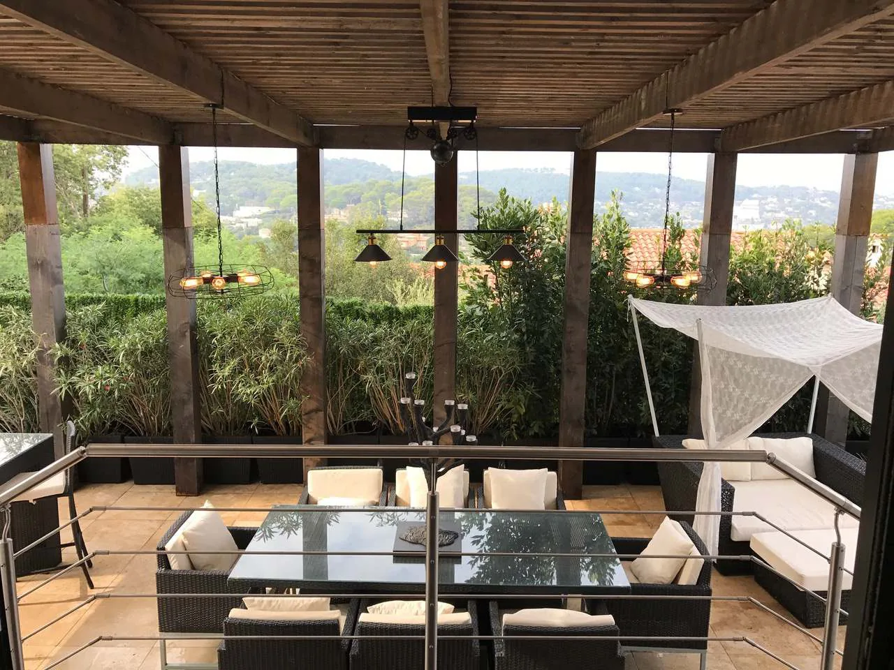 Pergola couverte avec salon outdoor en rotin noir, suspensions industrielles et vue sur les collines