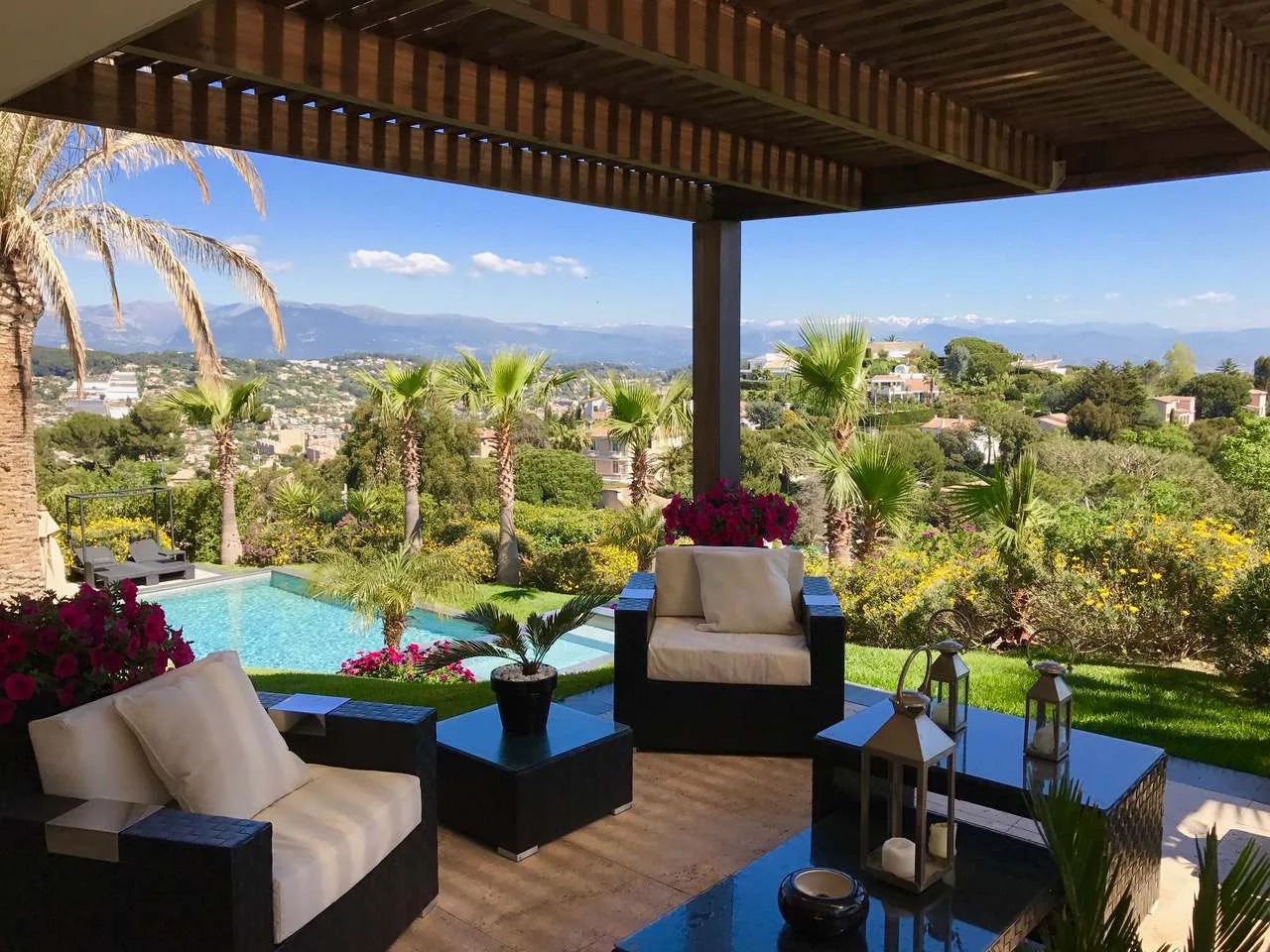 Salon de detente sous pergola avec vue panoramique sur le jardin tropical, la piscine et les montagnes enneigees