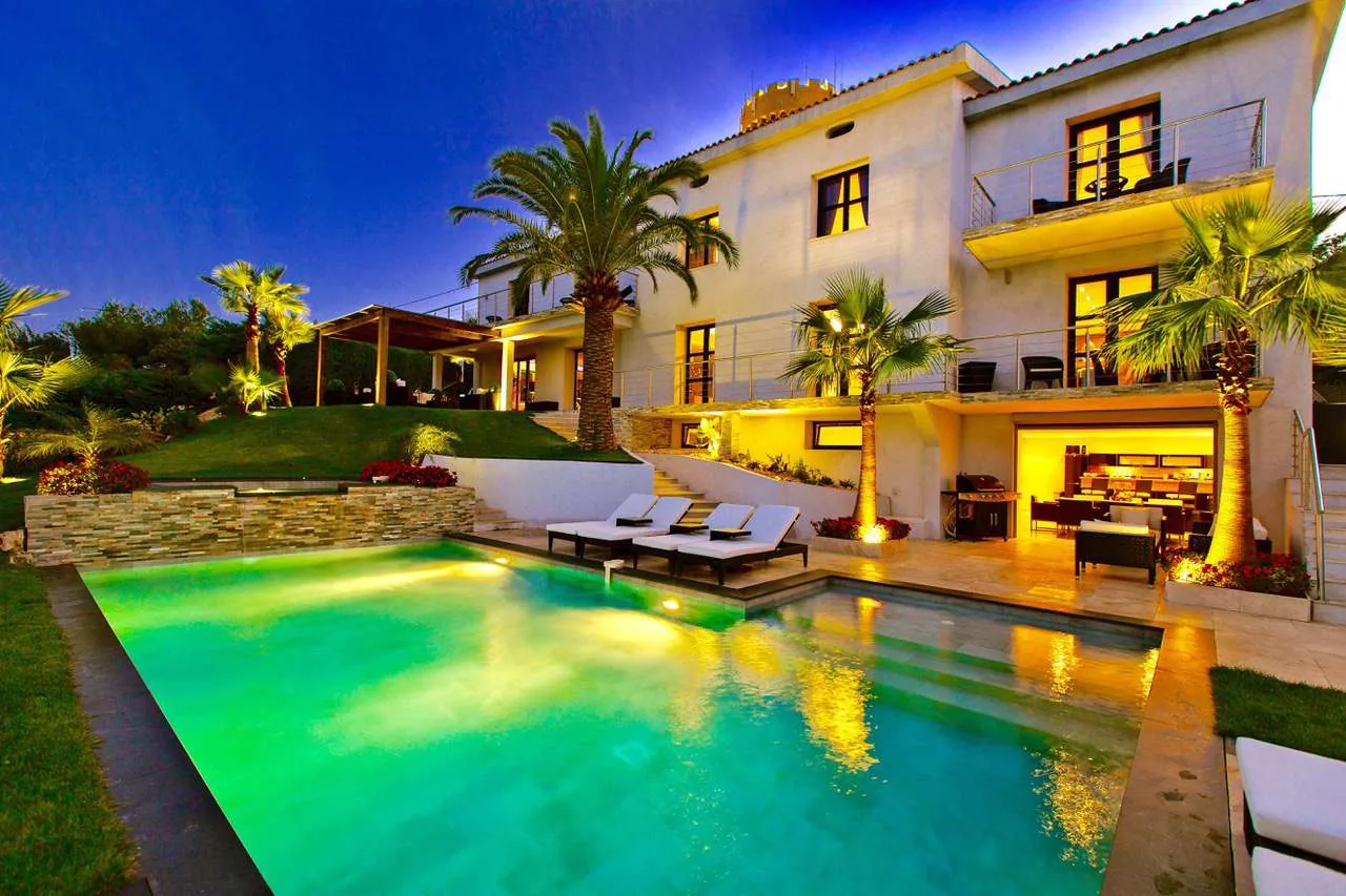 Facade arriere contemporaine de la Villa Belvedere illuminee la nuit avec piscine, pool house et palmiers