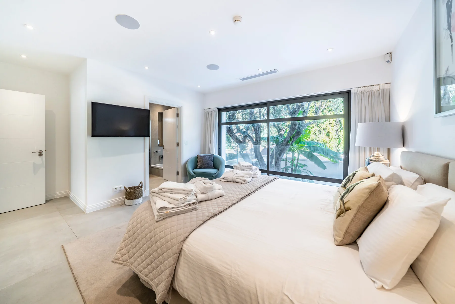 Chambre romantique avec fauteuil vert d'eau et baies vitrées sur jardin