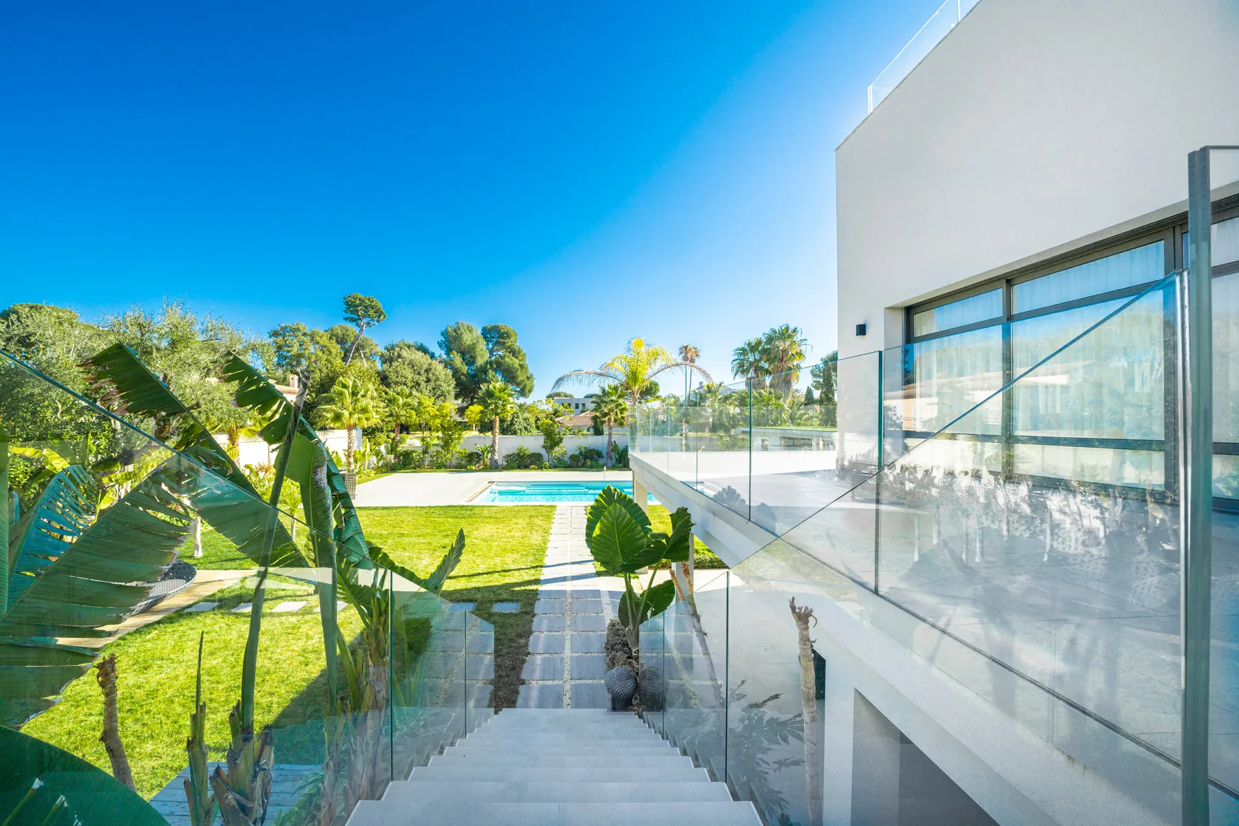 Jardin paysagé avec garde-corps verre, escalier extérieur et bananiers