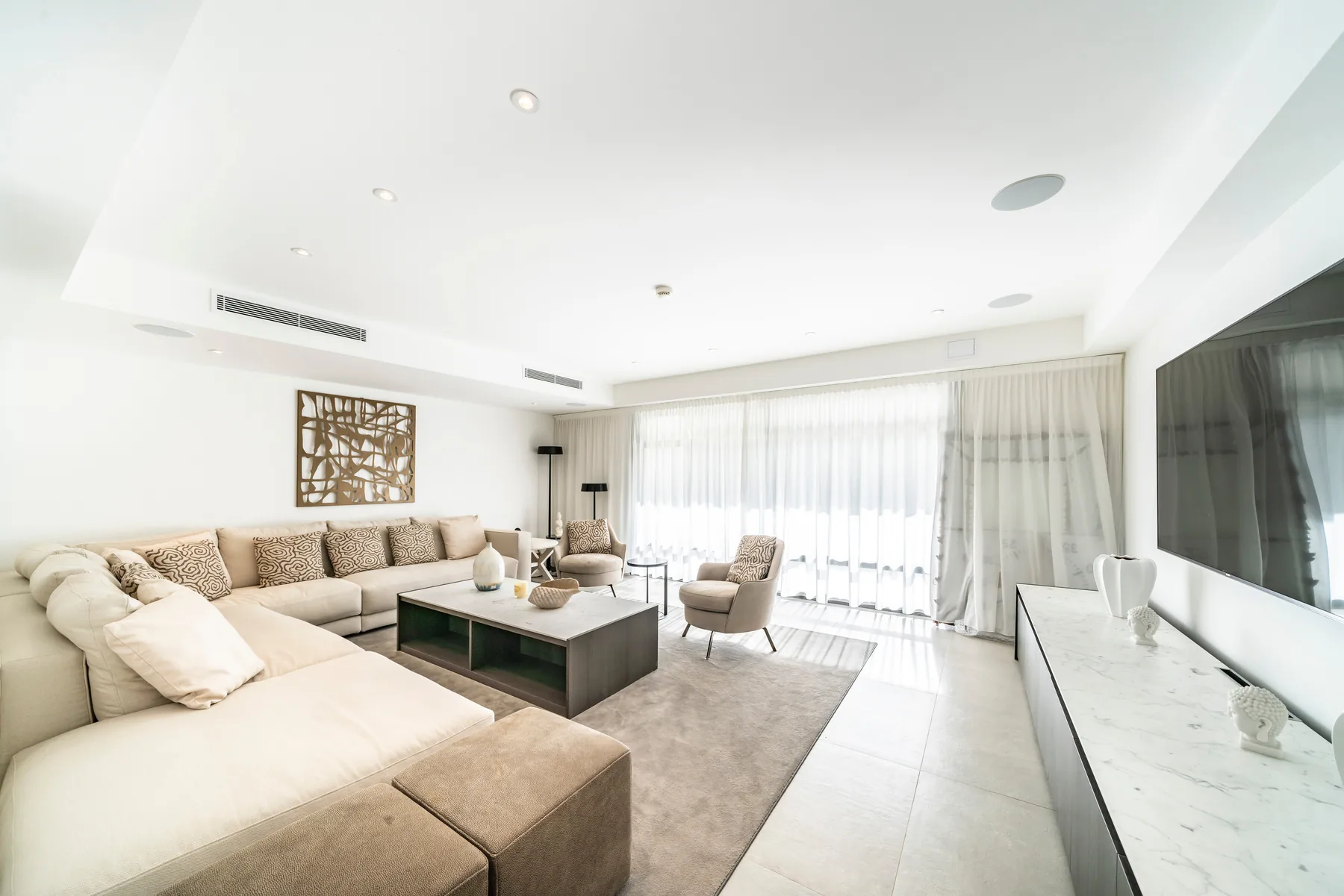 Lounge familial avec canapés beiges, TV grand format et baies sur jardin