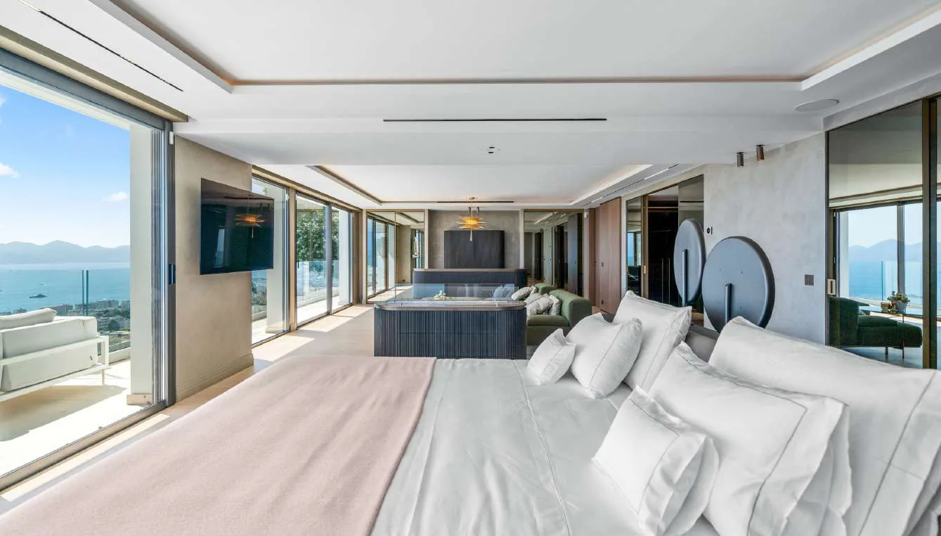Suite parentale longue vue : lit, salon TV et baies vitrées sur la mer