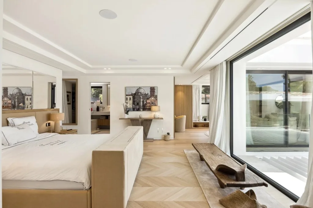 Suite parentale avec parquet chevron clair, lit et baie vitrée sur terrasse