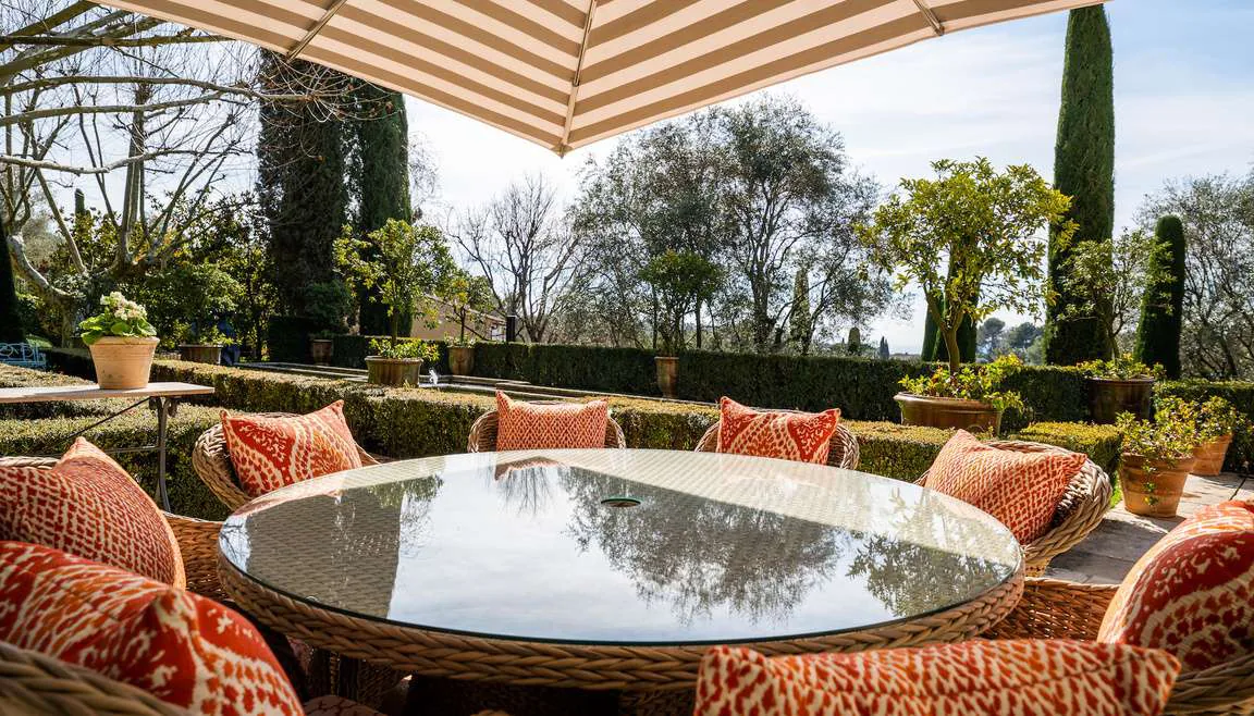 Terrasse de diner exterieur avec parasol raye et fauteuils en rotin