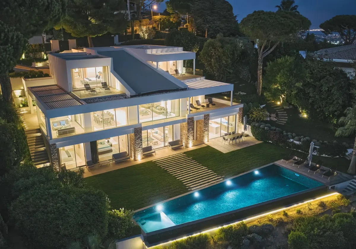 Façade entièrement illuminée la nuit avec piscine et jardins