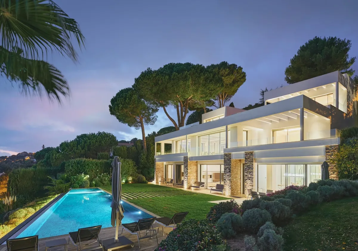 Villa illuminée au crépuscule avec piscine et pins parasols